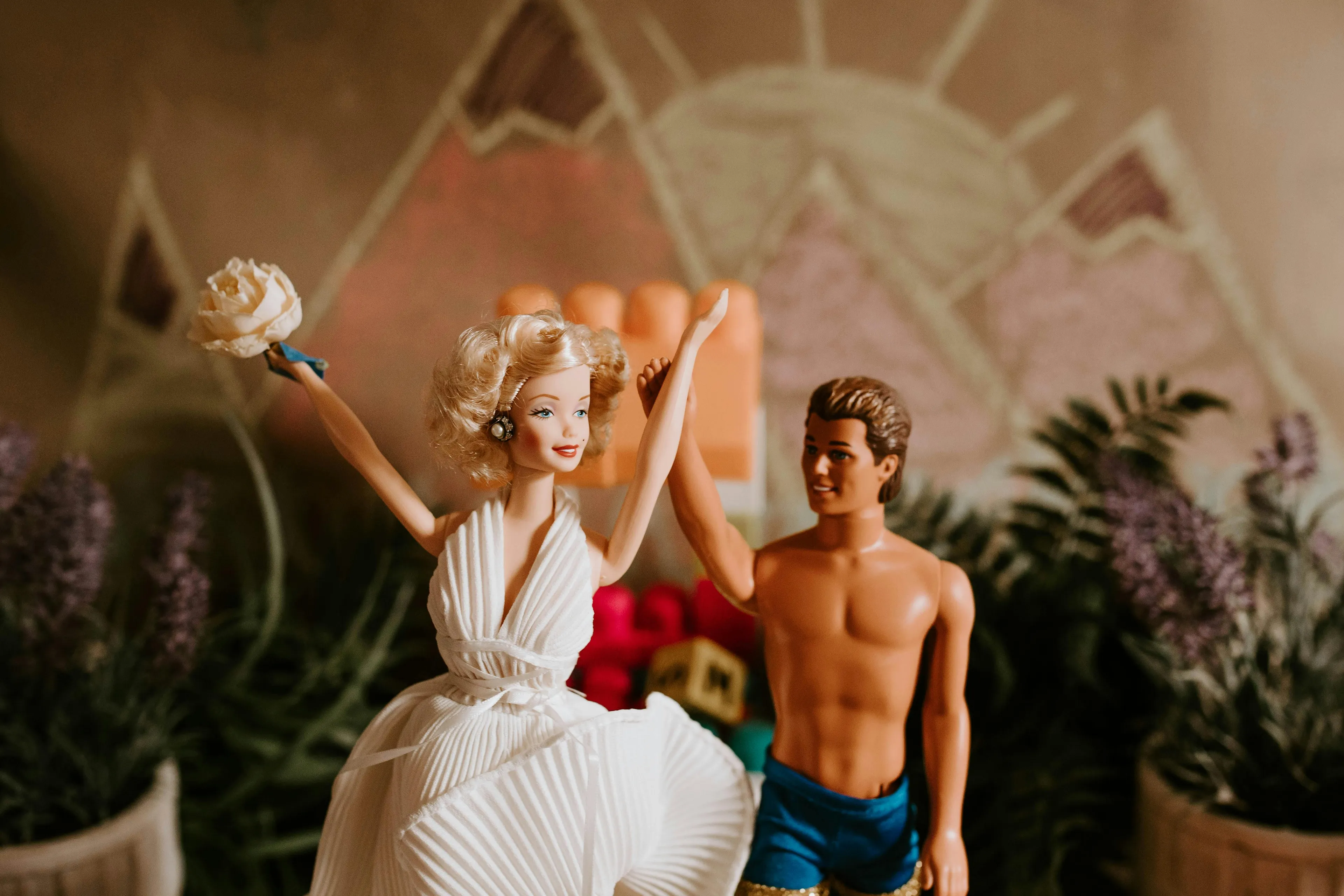 Barbie and Ken dolls posed with arms raised against a decorative floral and geometric background.