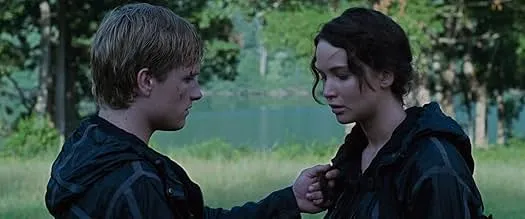 Two teenagers in dark clothing face each other outdoors, portraying a tense moment from The Hunger Games survival competition.