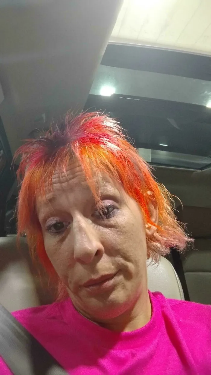 Person with uneven, vibrant orange and pink hair, showing a regrettable hair accident in a car seat.