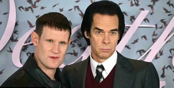 Two men with unusual and tragic haircuts posing against a backdrop with artistic lettering and birds.