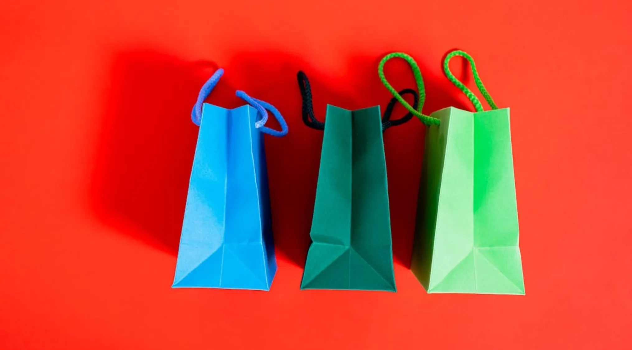 Three colorful bags in blue, teal and green on a bright red background representing basic math skills concept.