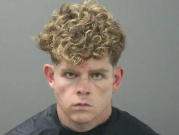 Young man with uneven curly hair and serious expression showing a tragic hair accident after a hairstylist visit.