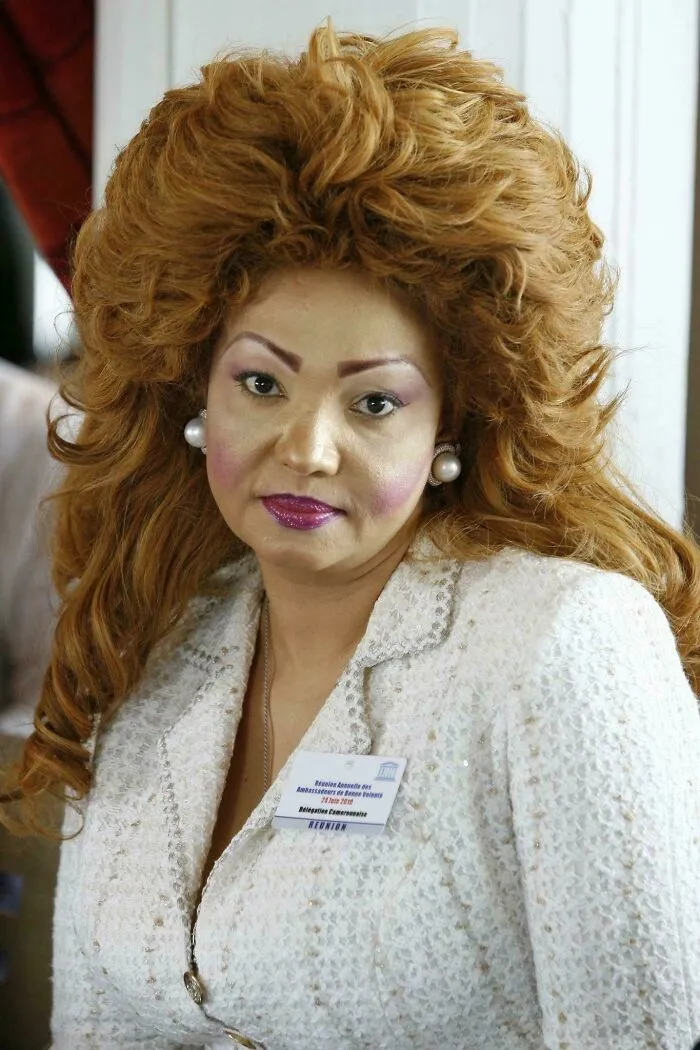 Woman with a dramatic tragic hair accident hairstyle, heavy makeup, and pearl earrings at an indoor event.