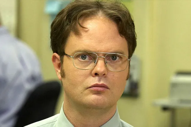 Dwight Schrute from old sitcom The Office wearing glasses and a green shirt with a serious expression in an office setting
