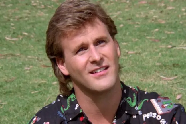 Uncle Joey from old sitcom sitting outdoors on grass, smiling and wearing a colorful patterned shirt.