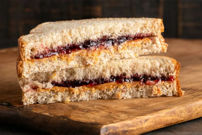 Peanut butter and jelly sandwich on whole wheat bread stacked on a wooden cutting board nostalgic snack.