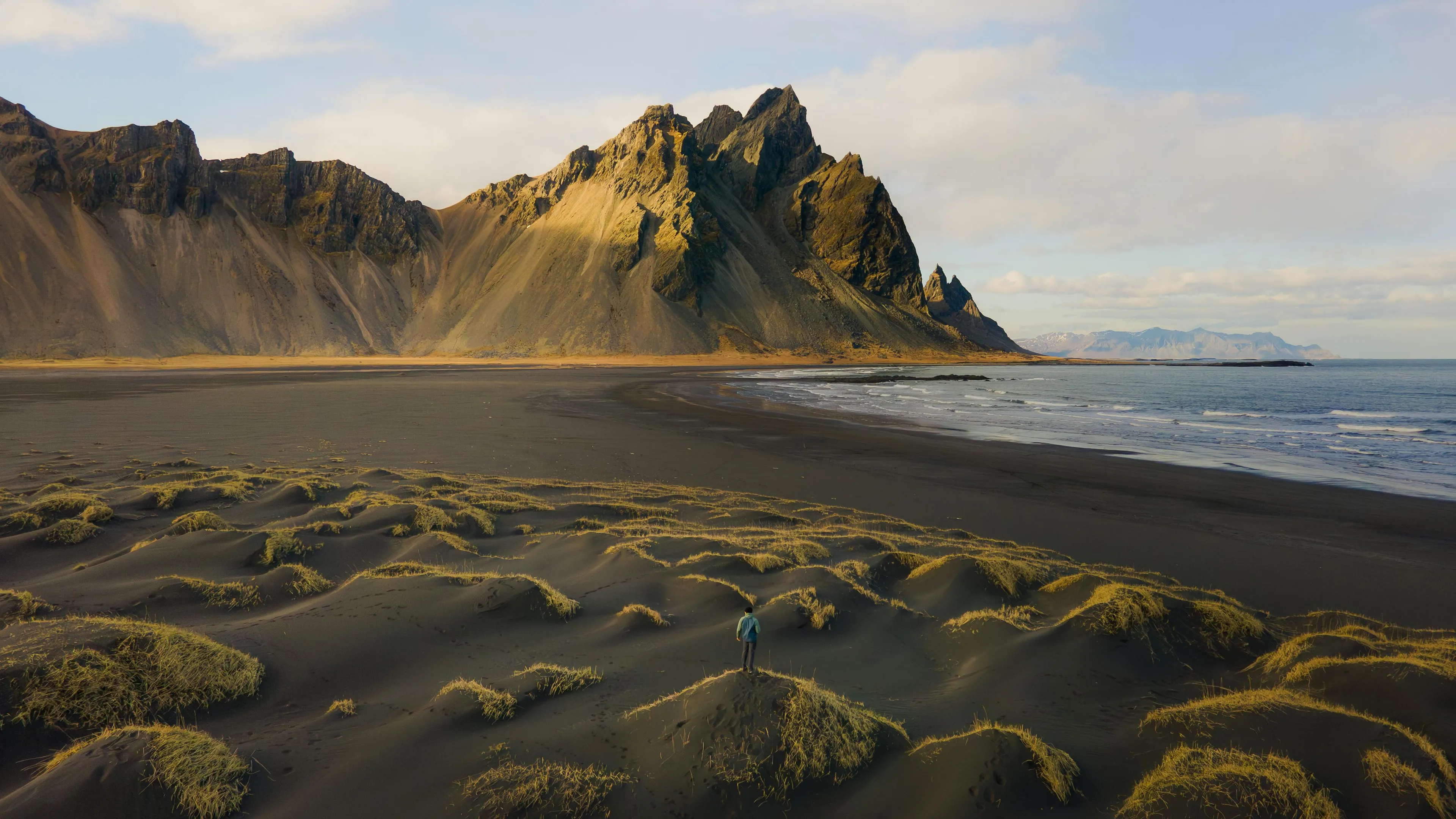 Person standing on black sand dunes near mountains by the ocean in Iceland, general knowledge quiz setting.