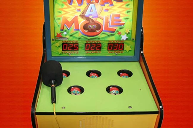 Whac-A-Mole arcade game with colorful moles popping up and a mallet ready for play on a green game surface.