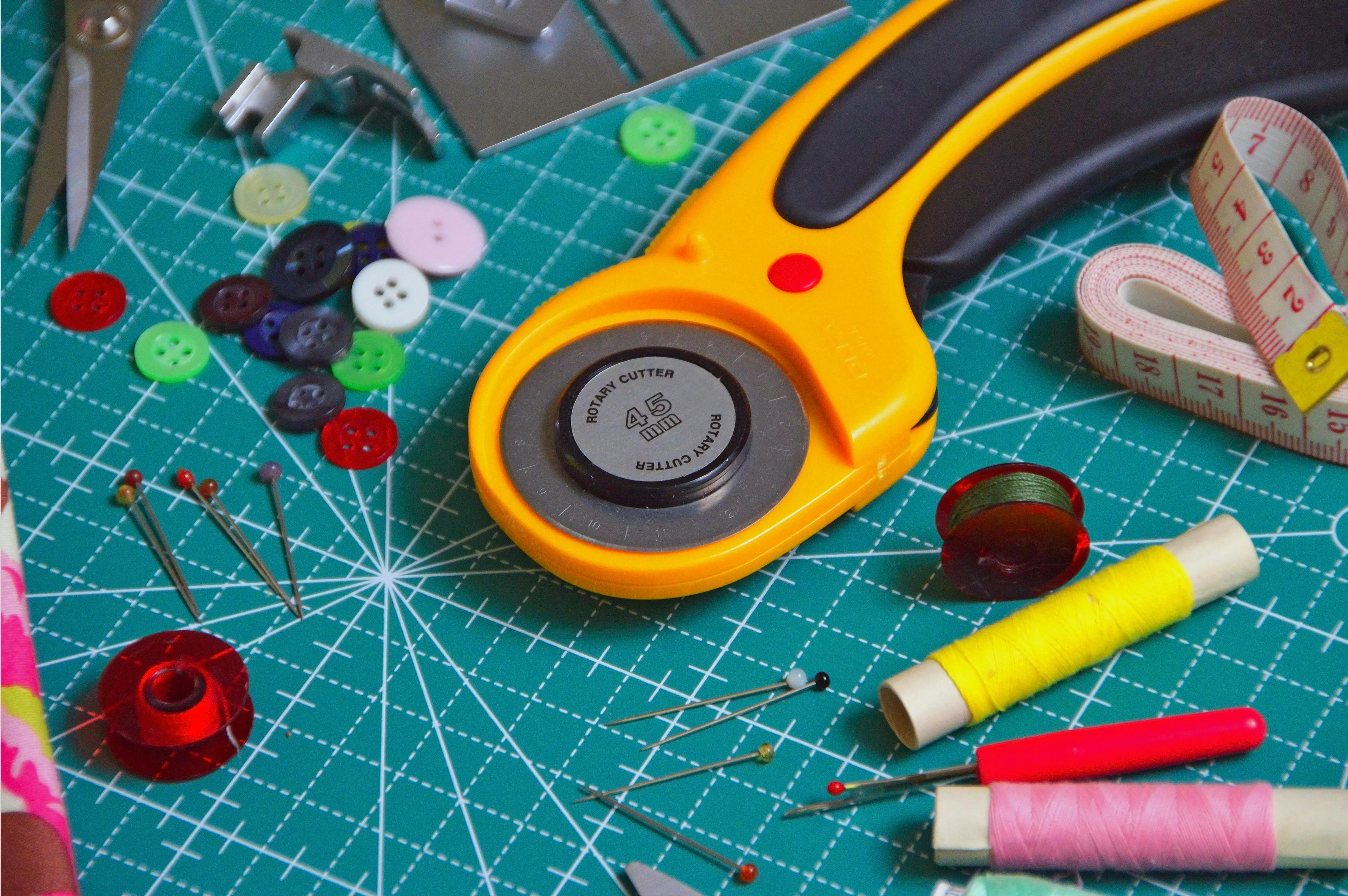Rotary cutter, sewing threads, pins, and measuring tape on a cutting mat for a weekend DIY project.