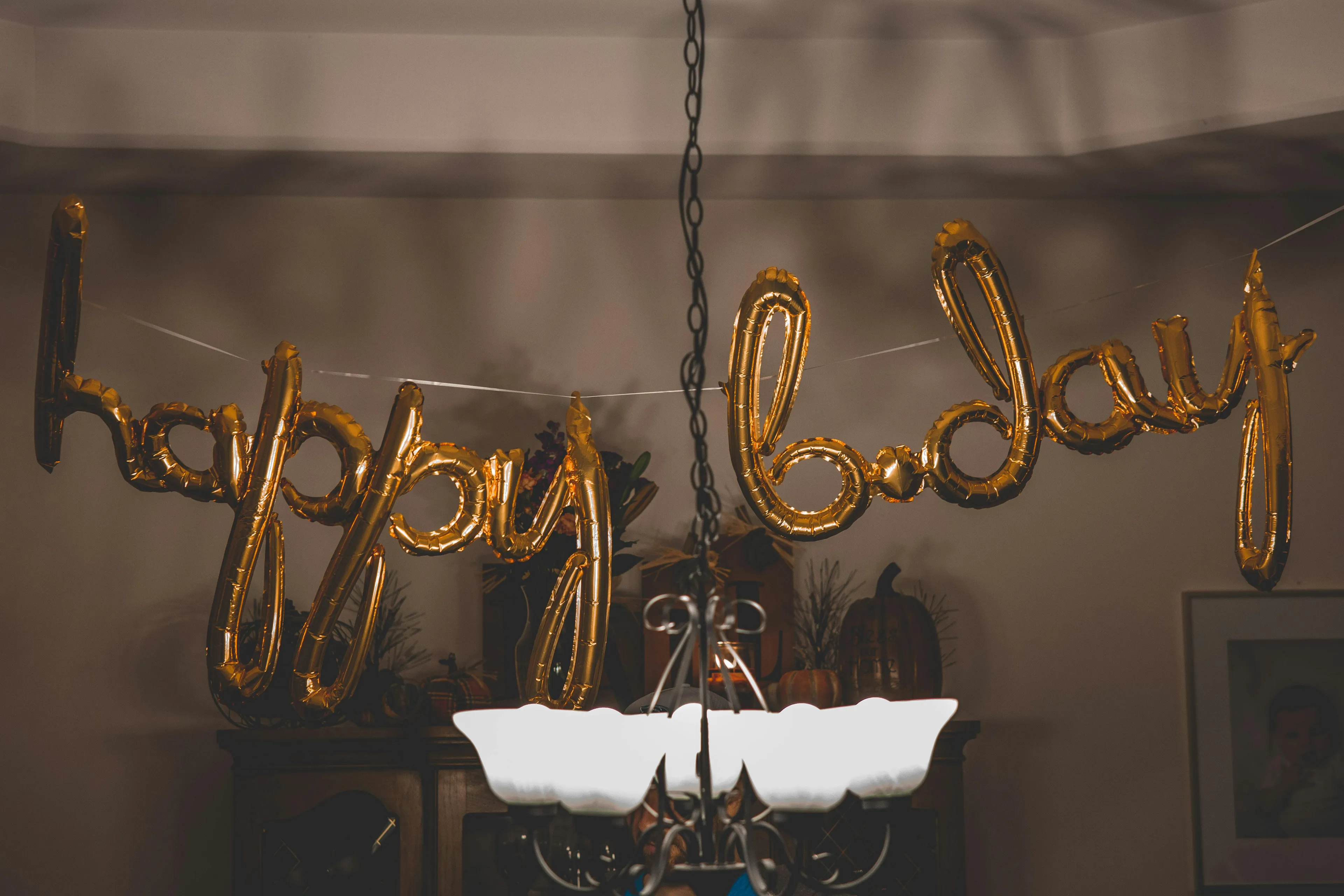 Gold balloon letters spelling happy birthday hanging in a dim room, illustrating psychological defense mechanism concept.