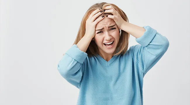 Young woman in blue sweater shows psychological defense mechanism reacting to unexpected bill with stress and frustration.