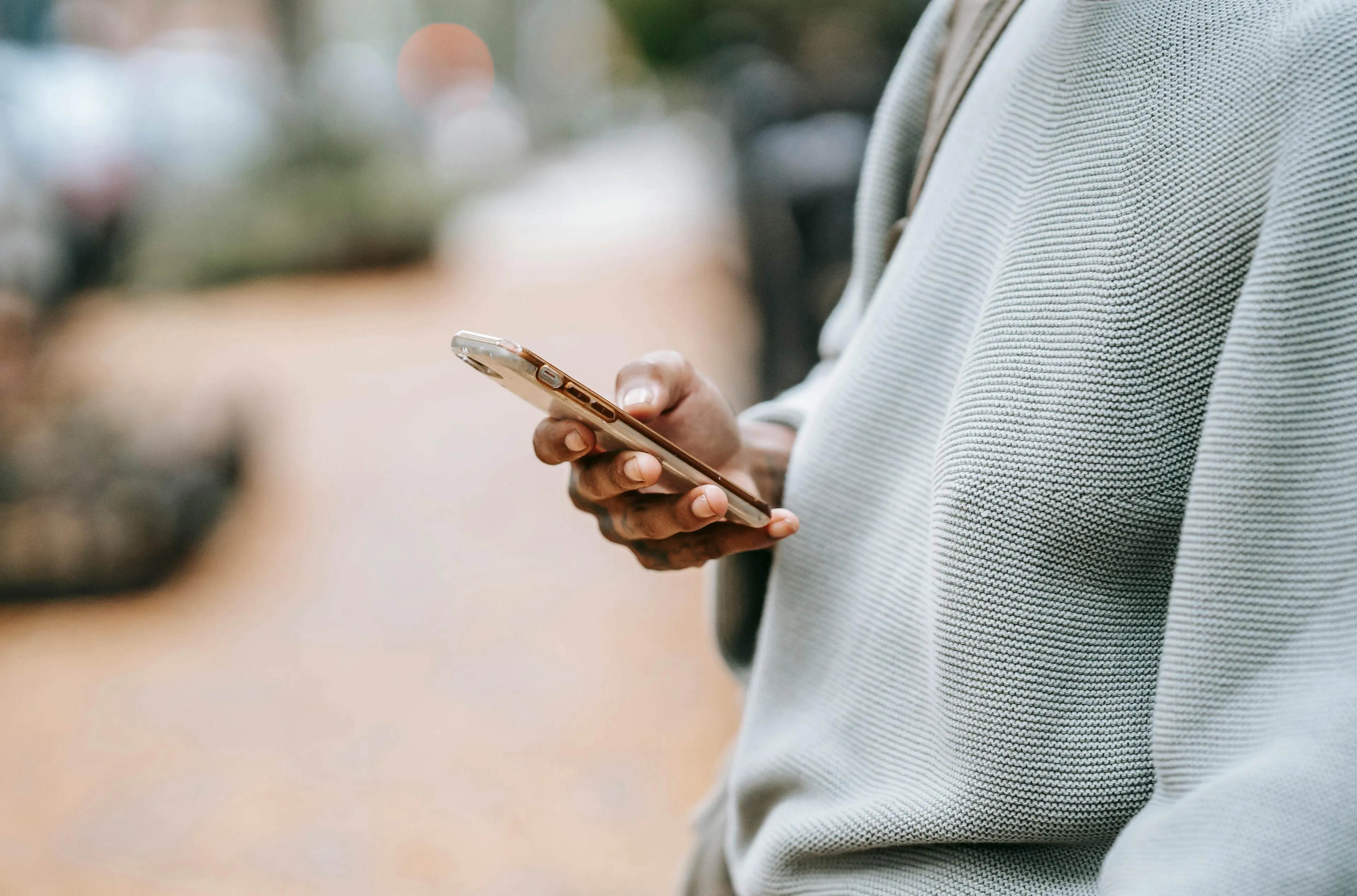 Person wearing a gray sweater holding a smartphone outdoors, illustrating psychological defense mechanism of ignoring texts.