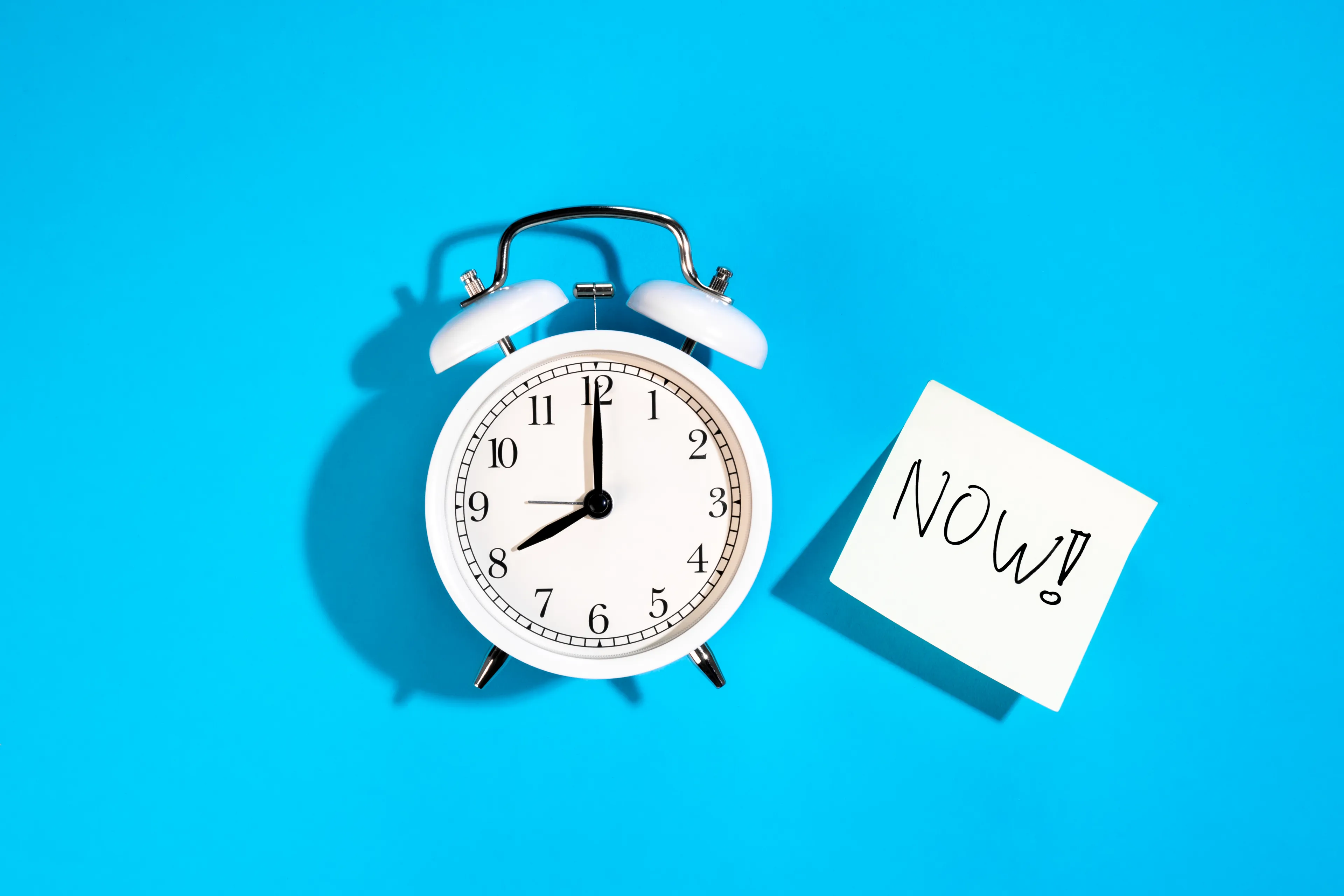 White alarm clock showing eight o'clock next to a sticky note with NOW, illustrating psychological defense mechanism concept.