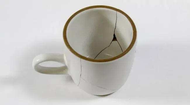 Cracked white ceramic mug showing psychological defense mechanism through visible fractures and damage.