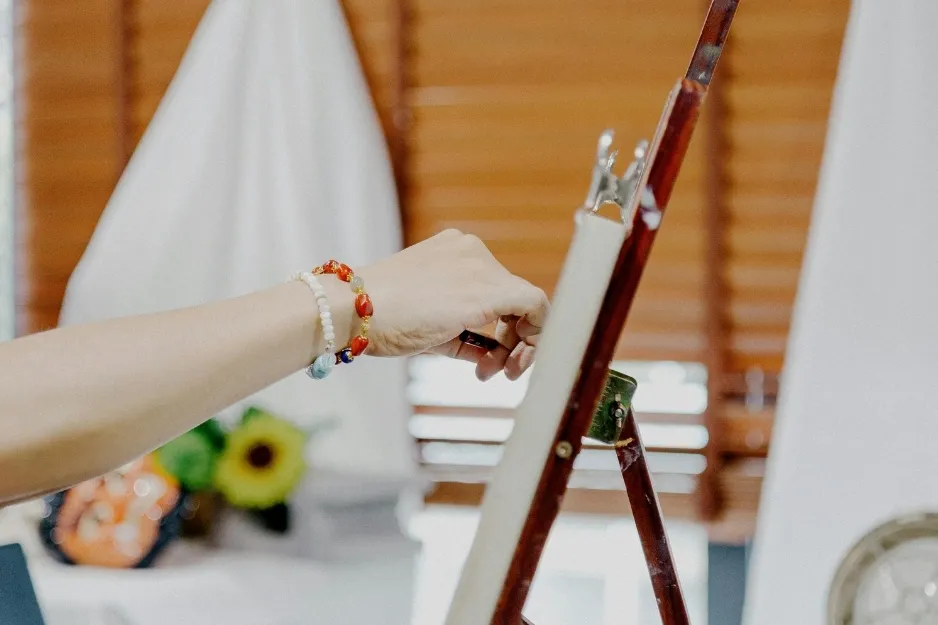 Hand adjusting canvas on easel, preparing a canvas for oil colors in a bright artist studio setting.