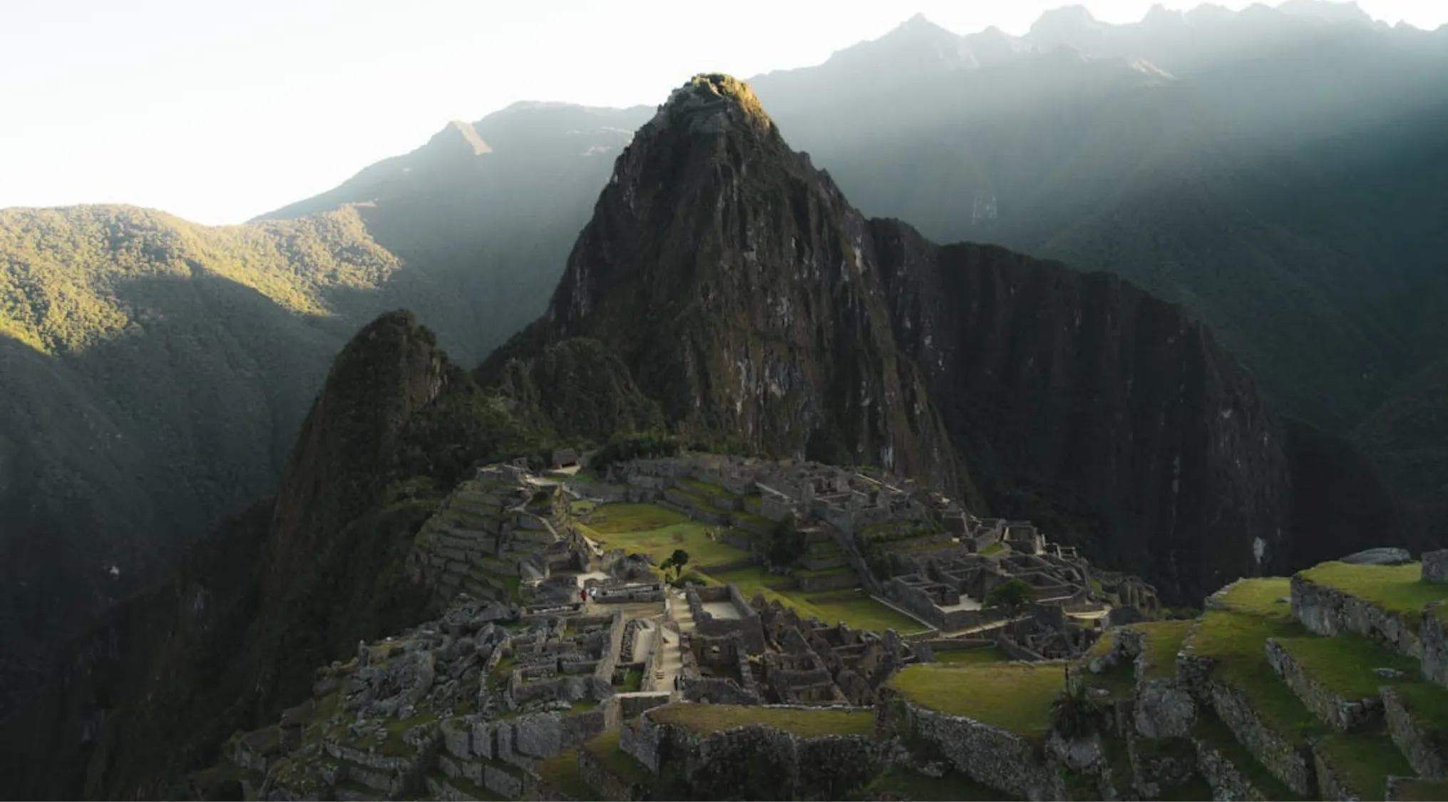 Machu Picchu ancient stone ruins with surrounding mountains in Peru, South America at sunrise with soft light and shadows.