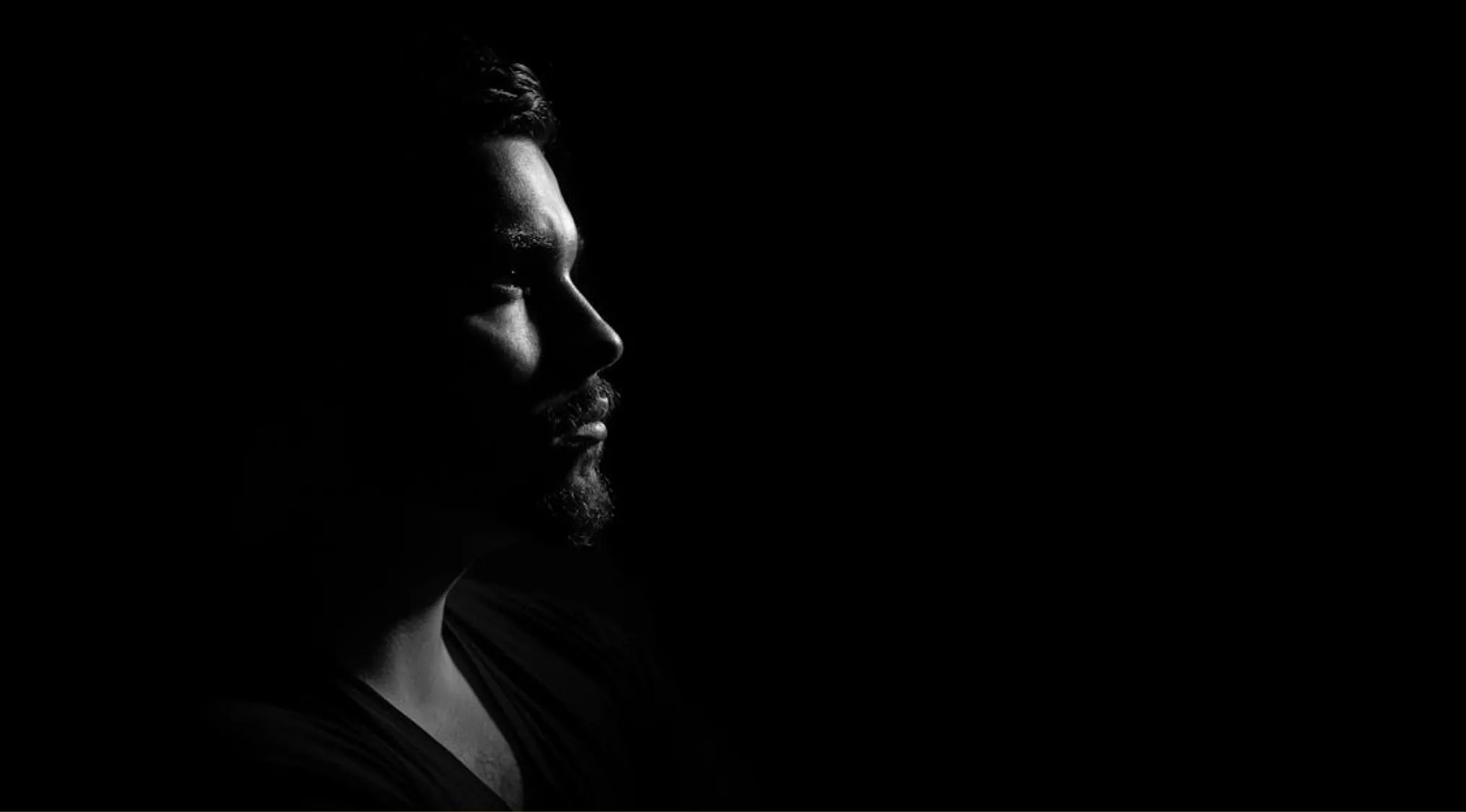 Side profile of a man in low light highlighting the skin, the largest organ in the human body, against a black background.