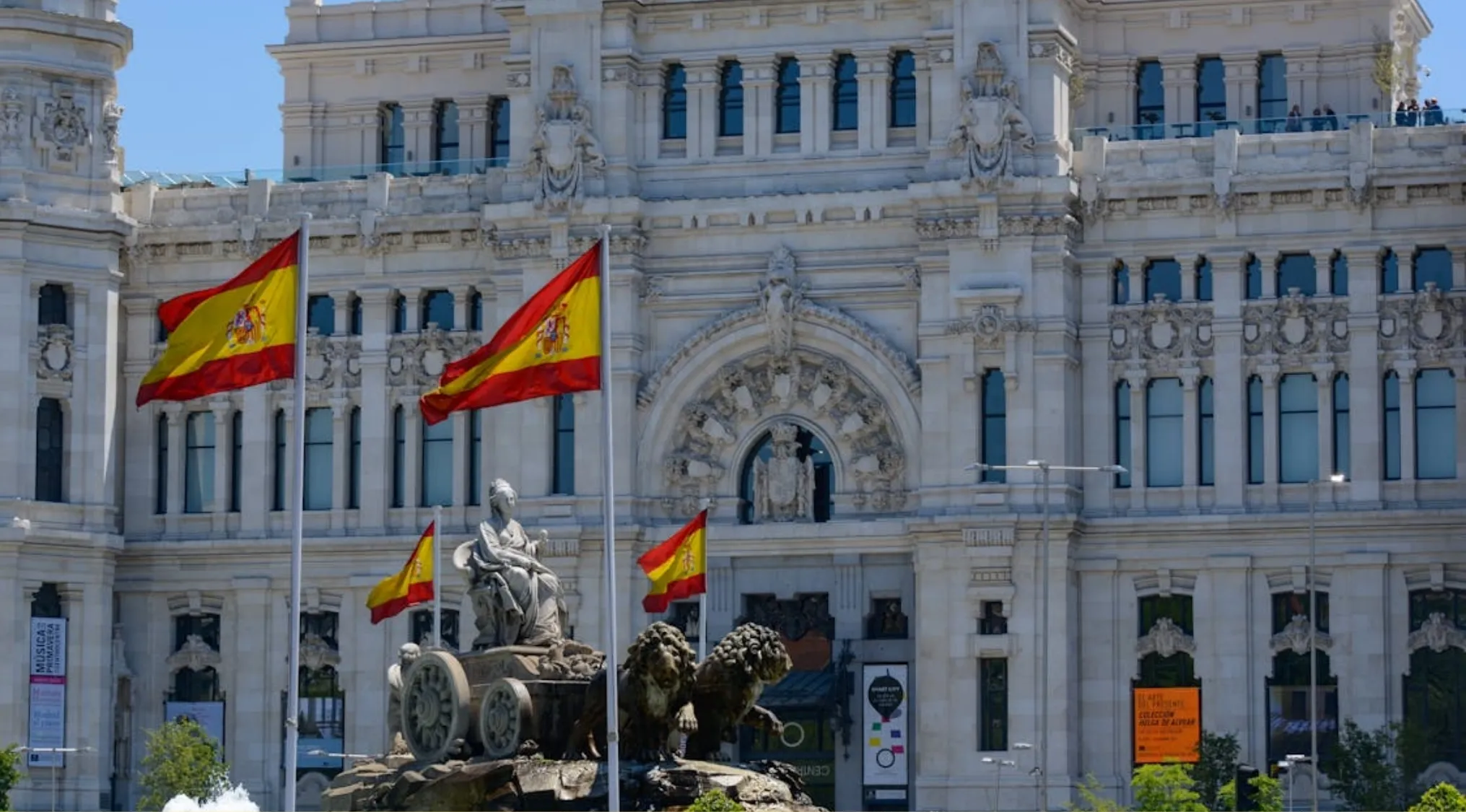 Statue and Spanish flags in front of historic architecture showcasing the capital city of Spain, Madrid.
