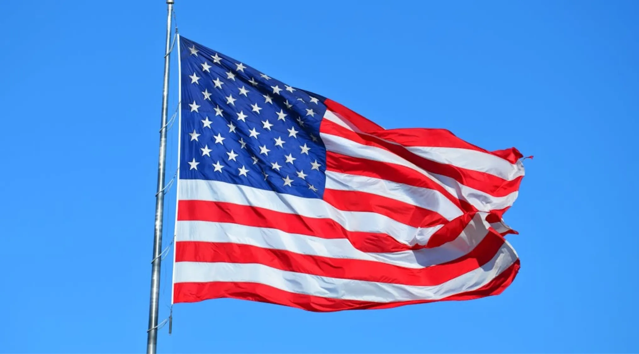 American flag waving against clear blue sky representing first President of the United States general knowledge quiz