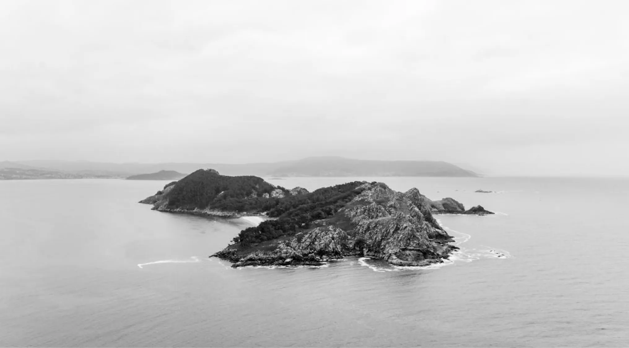 Rocky island covered with trees surrounded by calm sea waters under an overcast sky, largest island concept.
