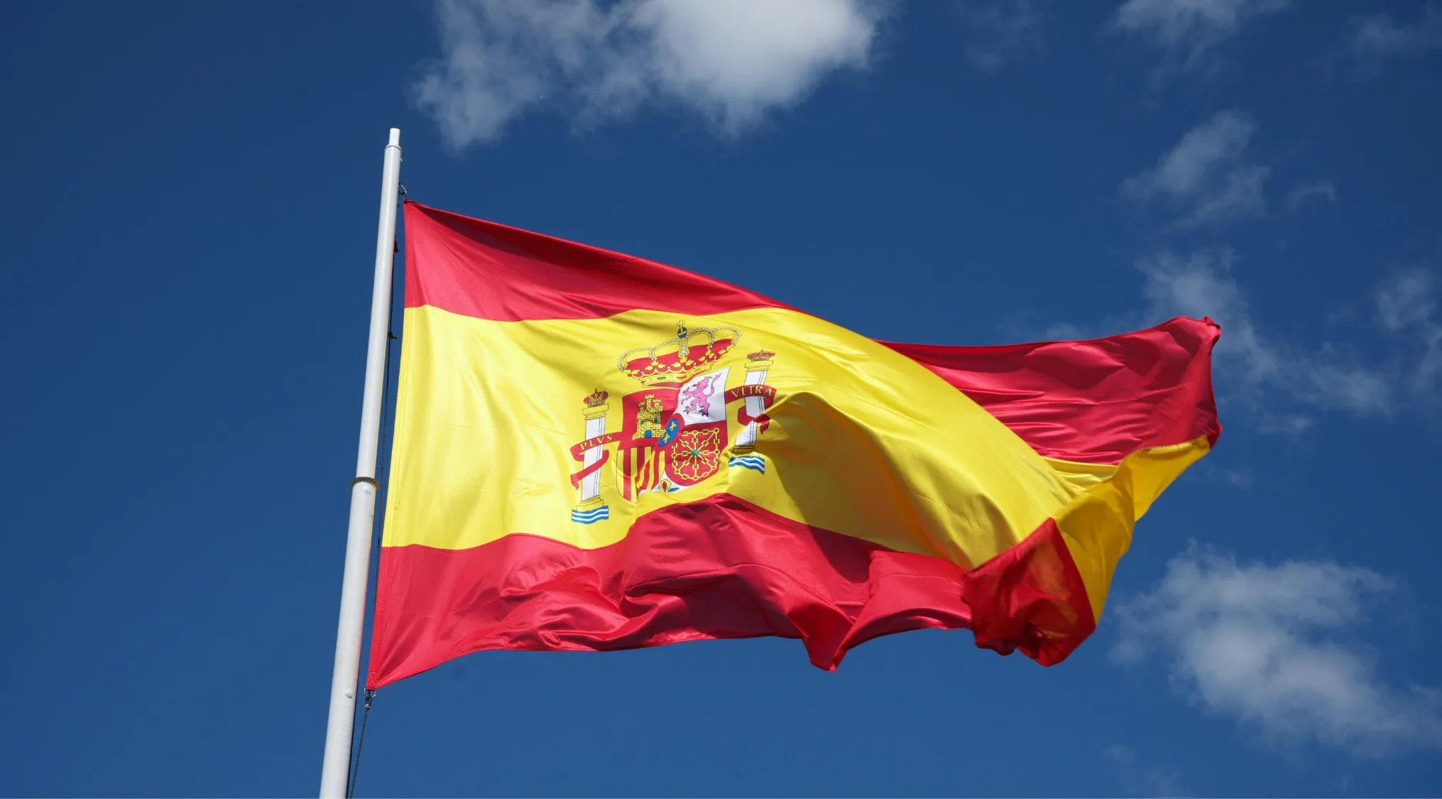 Spanish flag waving against blue sky, representing countries that are often mixed up with one being a city in Spain