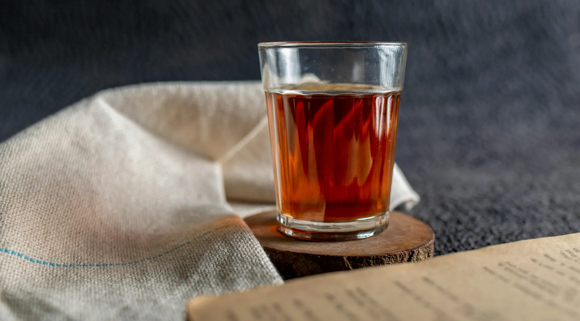 Glass of black tea on wooden coaster with cloth and book, illustrating statistics relative frequency concept in quiz.