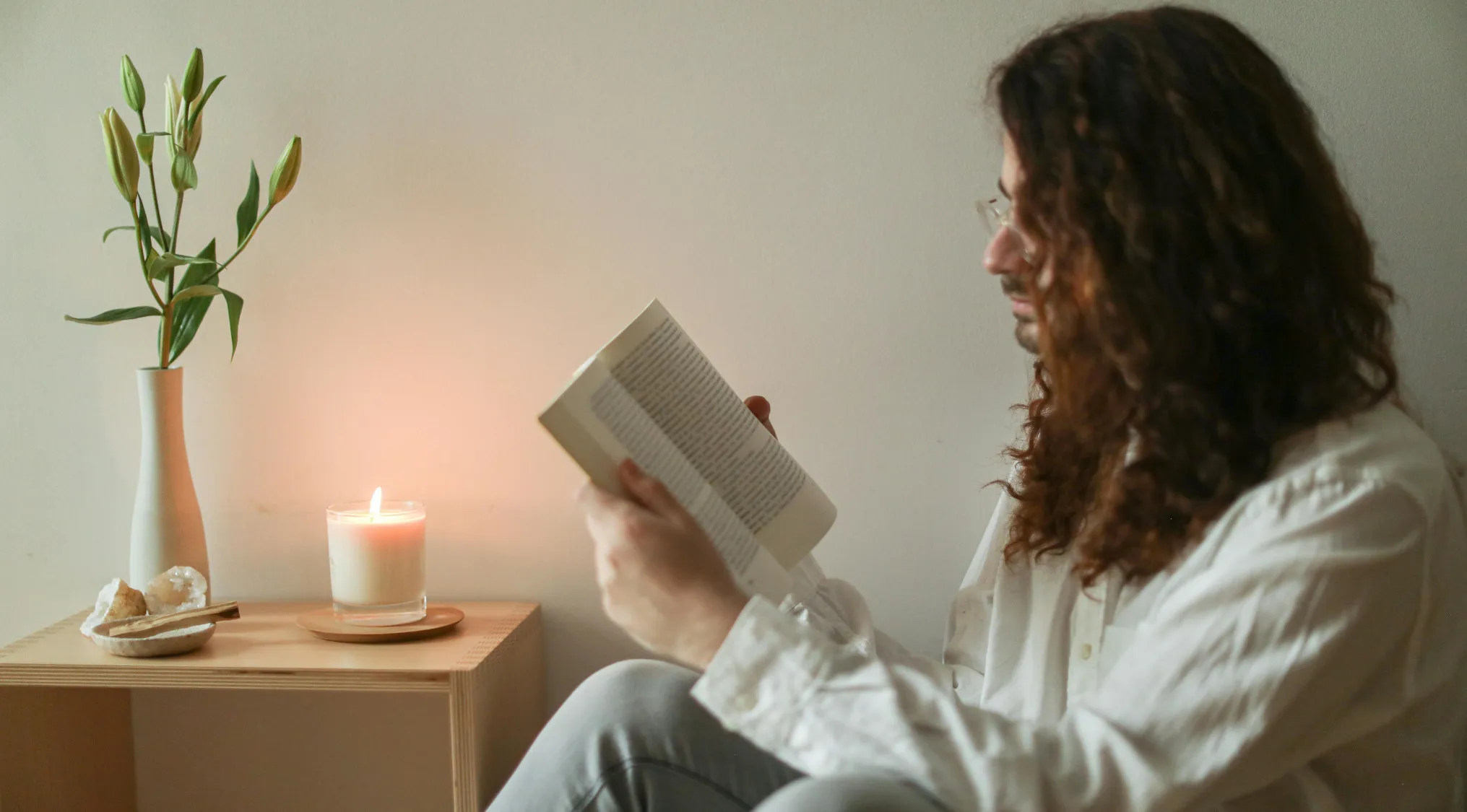 Person with curly hair reading a book in a calm space with a candle and plant, related to Advanced Placement school quiz.