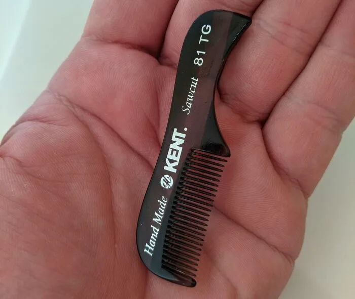 Pequeño peine negro Kent Sawcut en la palma de una mano, un ejemplo de herramientas geniales que simplifican tu vida.