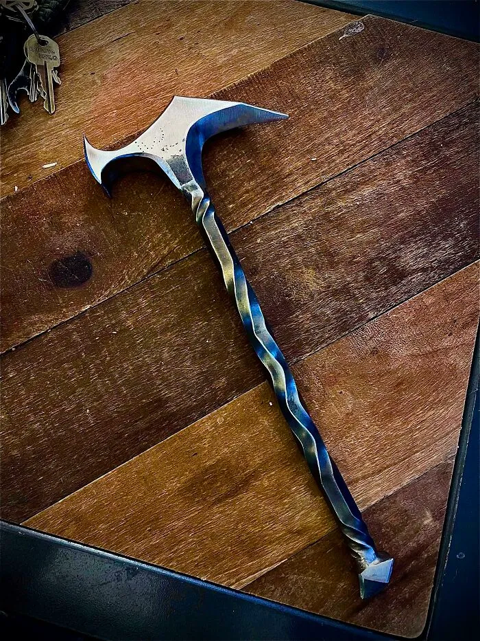 Twisted metal hammer with sharp, curved head showcasing metalworkers craftsmanship and remarkable design on wooden surface.
