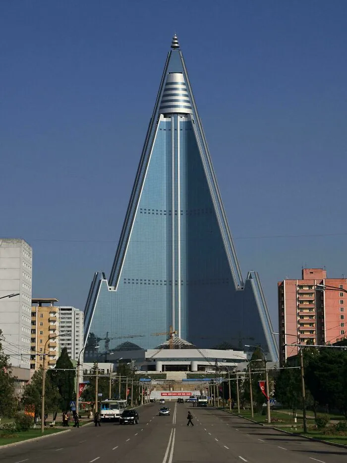 Pyramid-shaped skyscraper in a dystopian urban hell cityscape with surrounding residential buildings and street traffic.
