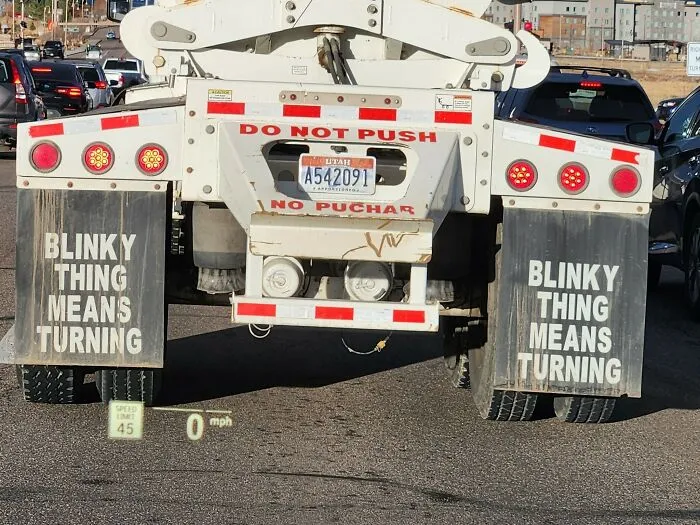 Rear view of a truck with strange signs on mud flaps stating blinky thing means turning on a busy road.