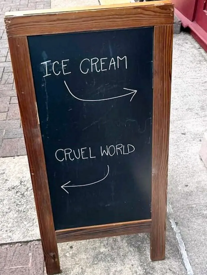 Chalkboard sign with arrows pointing right for ice cream and left for the cruel world, showcasing strange signs.