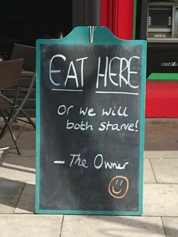 Chalkboard sign outside restaurant with a humorous message urging customers to eat here or both will starve.