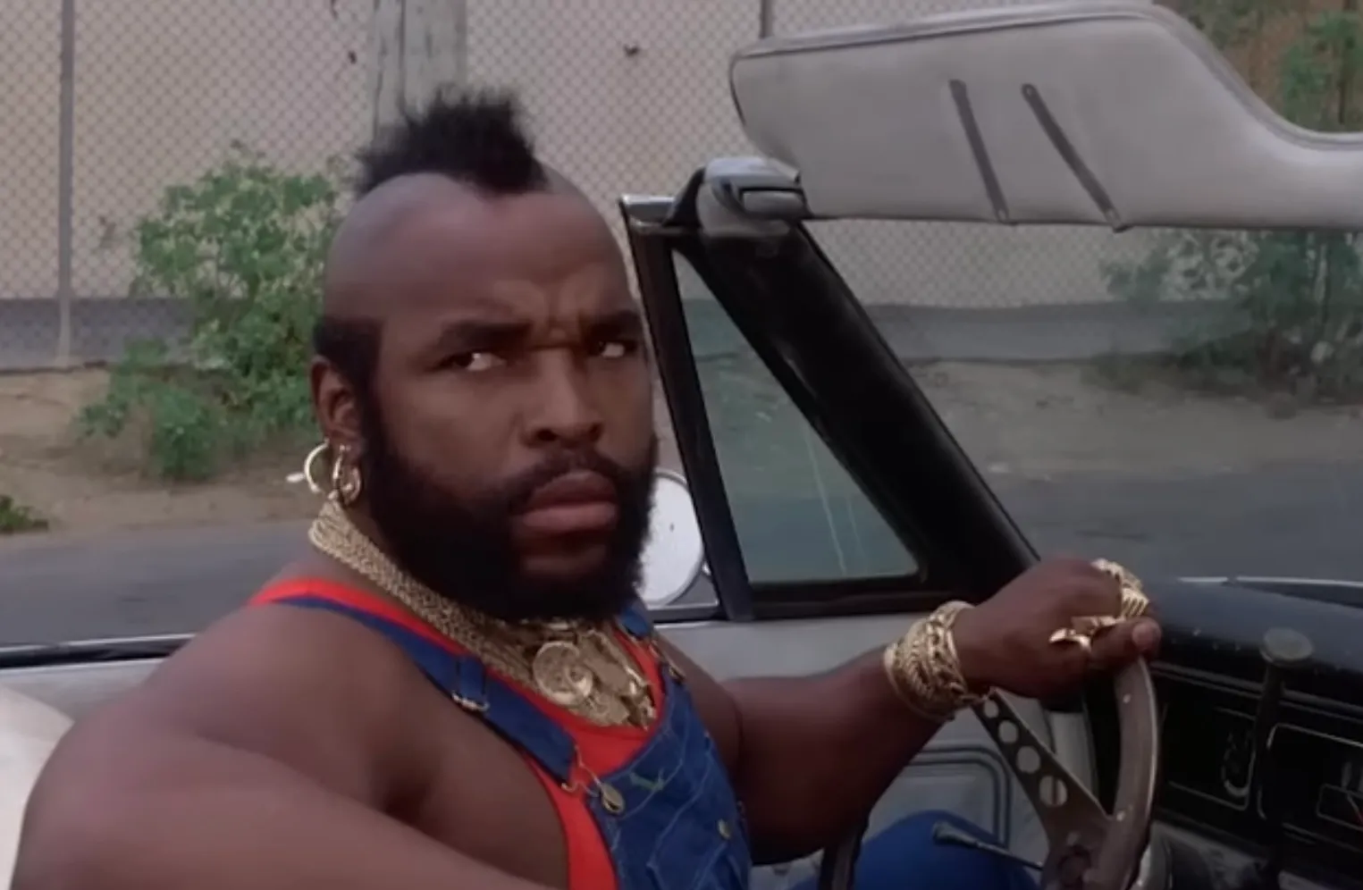 Mr. T in character from 1980s TV series The A-Team, wearing gold chains and driving a convertible car.