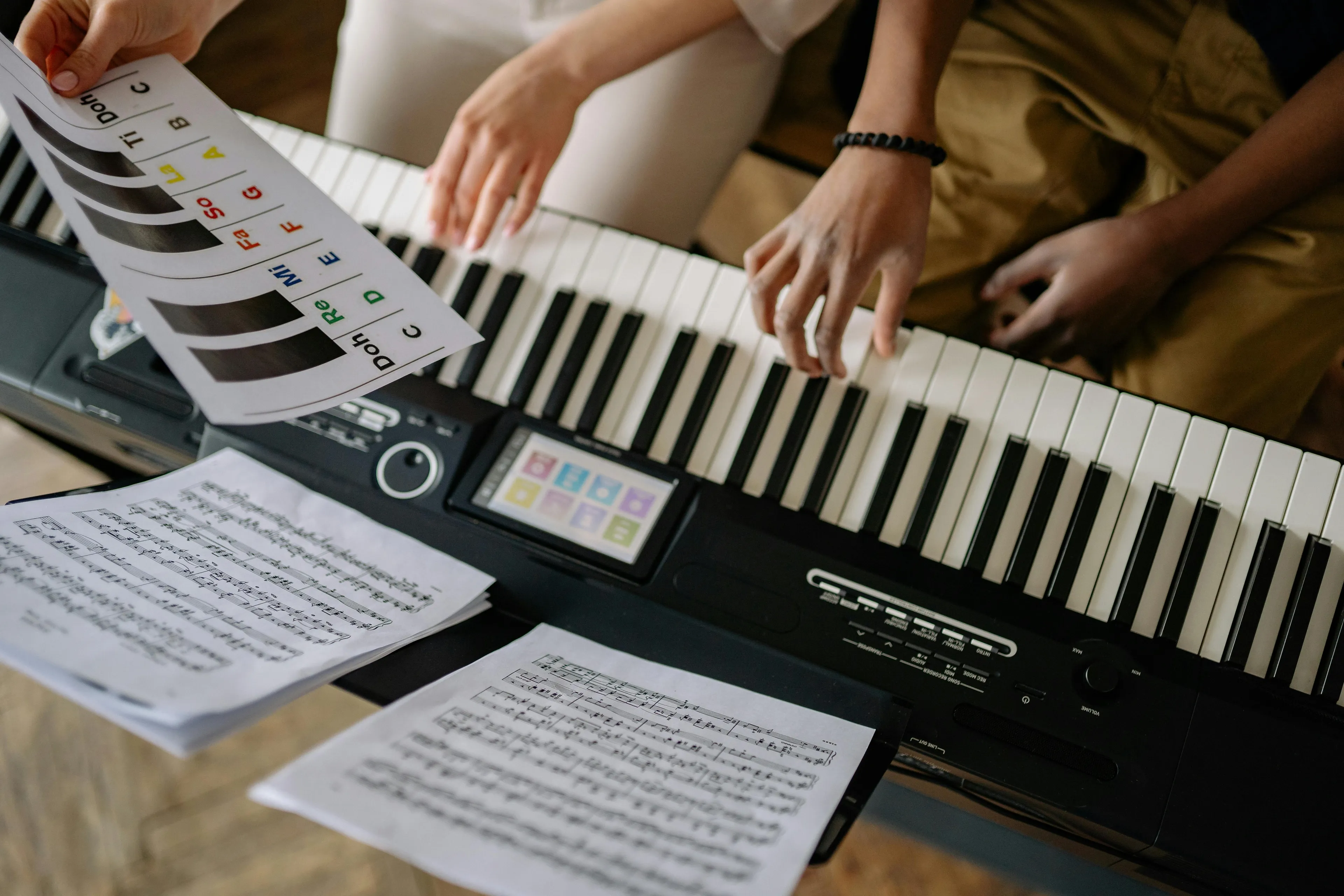 Hands playing keyboard with music notes and a colorful sheet showing compositional technique in music learning session.