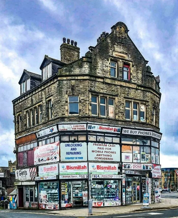 Dystopian urban hell scene showing a worn, crowded phone shop in an old, dilapidated city building under cloudy skies.