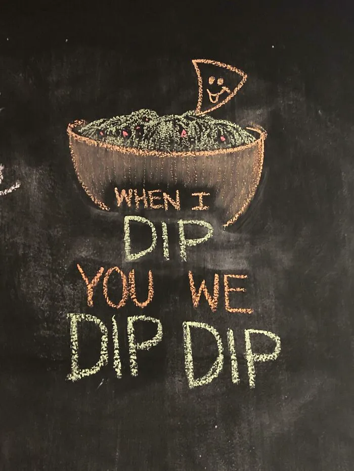 Chalkboard sign with a bowl of guacamole and a smiling chip, displaying a comedic dip pun.