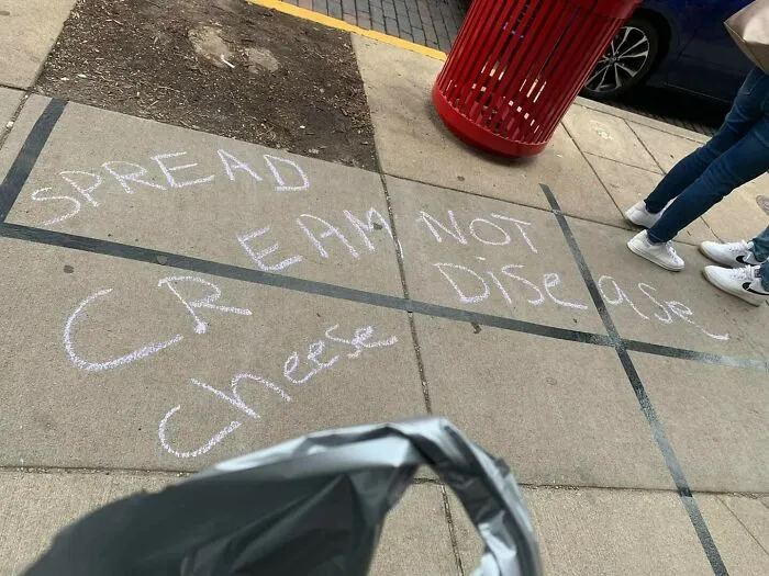 Sidewalk chalk sign with a misspelled message about spreading cream cheese instead of disease, a comedic sign fail.