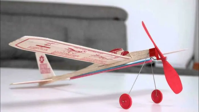A classic red and white balsa wood model airplane with a propeller and wheels, one of many images that take you way back.