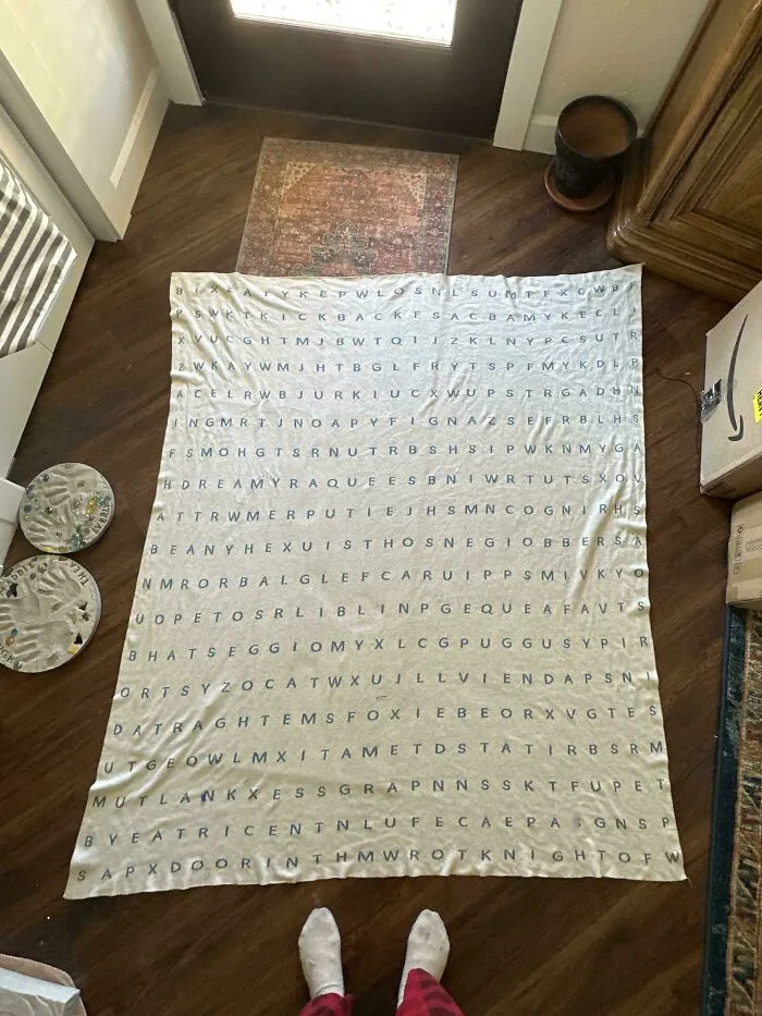 Large word search blanket laid on wooden floor, showcasing perfectly camouflaged letters that might take ages to find.