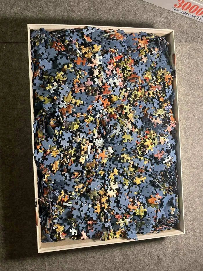 Box filled with thousands of puzzle pieces showing a perfectly camouflaged pattern that is challenging to find and assemble.