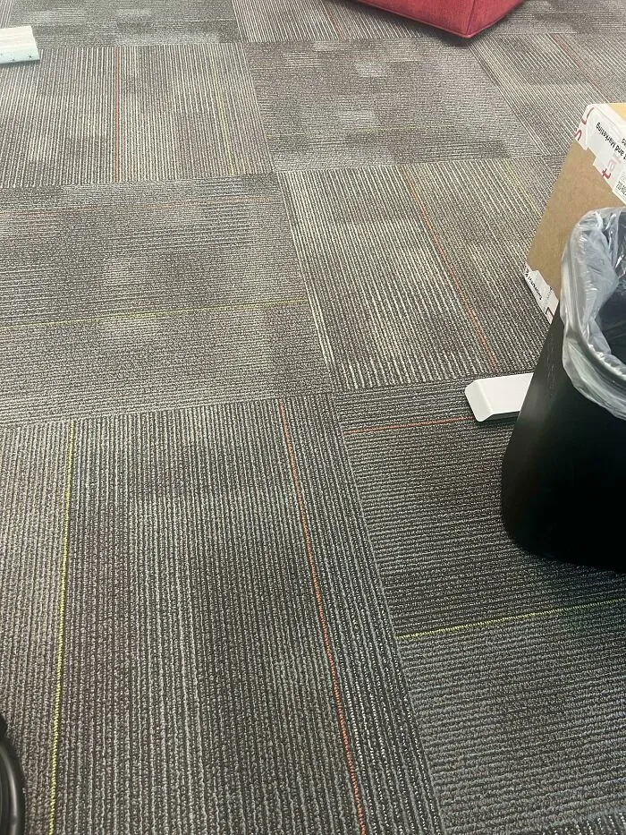 Gray office carpet with subtle colored lines camouflaging a nearly invisible smartphone blending into the floor pattern.