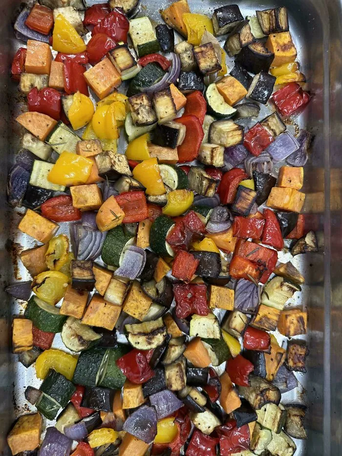 Roasted mixed vegetables including bell peppers, zucchini, sweet potatoes, and onions in a metal baking tray.