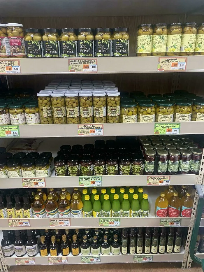 Shelf stocked with jars of various olives and bottles of vinegar, illustrating perfectly camouflaged things in a grocery store.