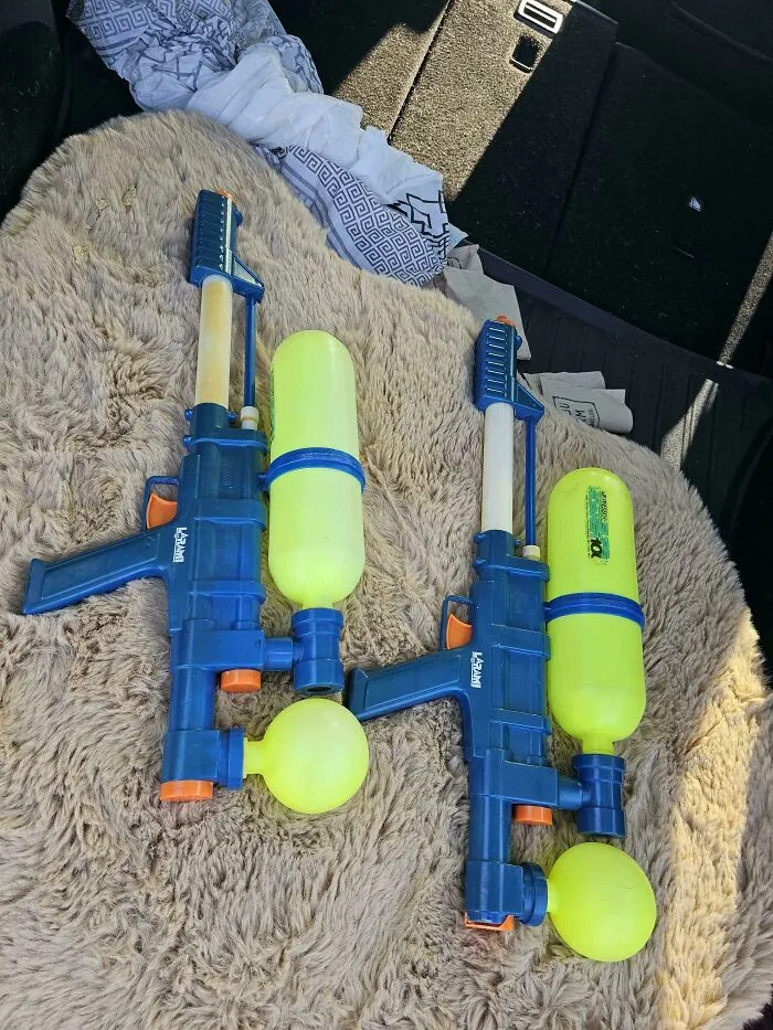 Two vintage 90s Super Soaker water guns lying on a brown furry blanket, evoking nostalgic kids toys memories.