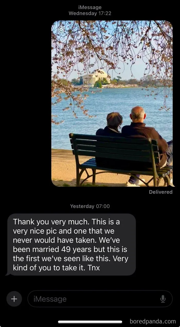 Elderly couple sitting on bench by water with cherry blossoms, pictured by a stranger