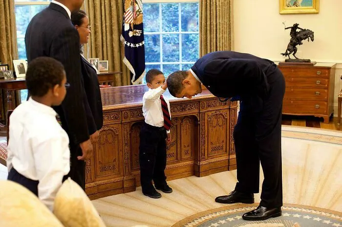 Child salutes an adult in a suit in a wholesome Oval Office moment