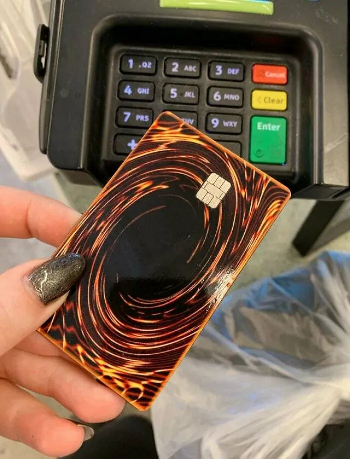 Hand holding a credit card designed like a Yu-Gi-Oh card near a payment terminal in a weird and confusing image.