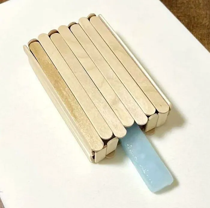 Blue popsicle with wooden sticks arranged vertically on a white surface creating a weird, confusing, and cursed image.
