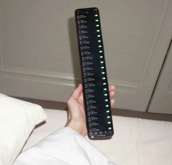 Hand holding a stretched smartphone screen showing multiple alarm times all turned on in a confusing layout.